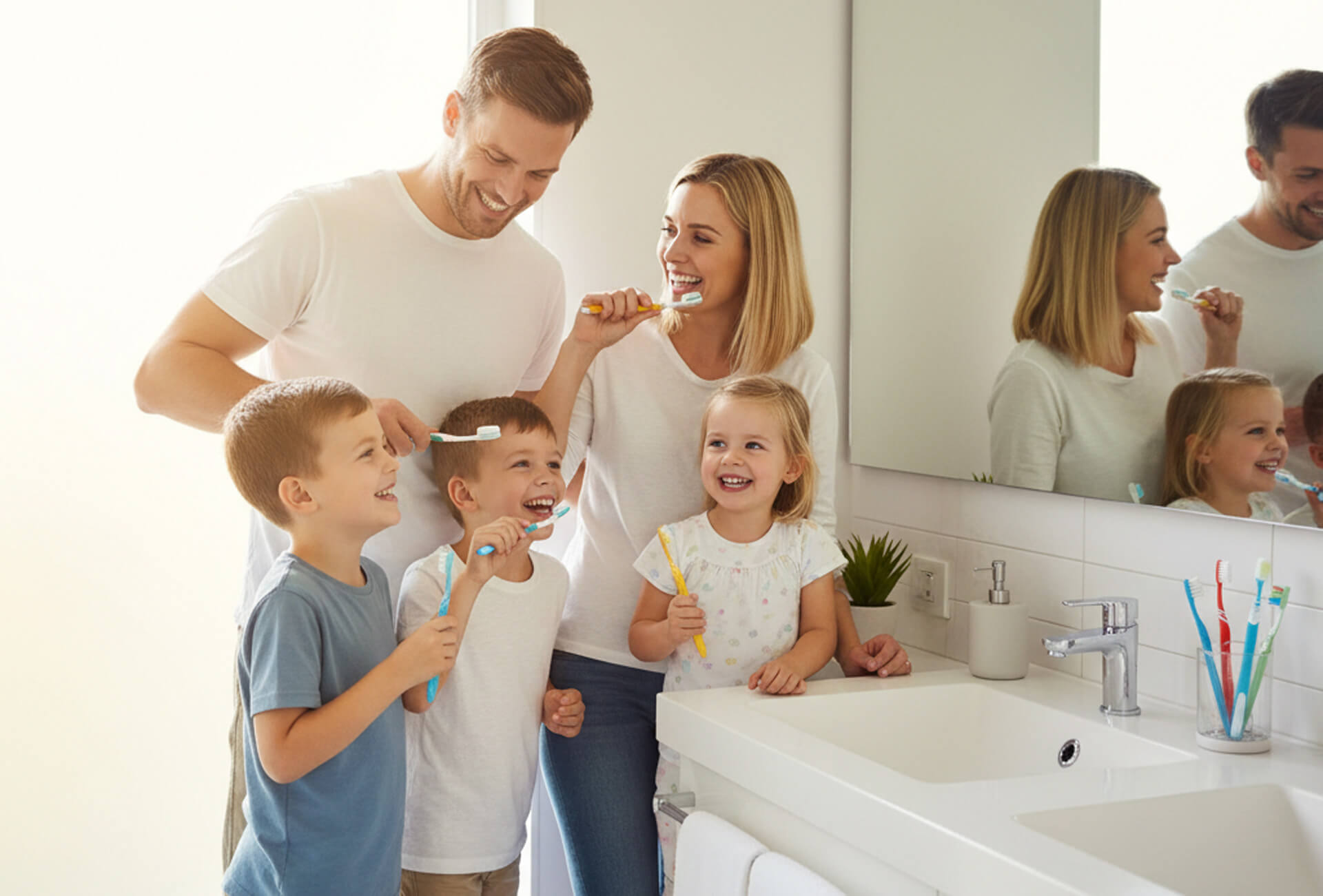 Family brushing teeth together in a bathroom, promoting dental hygiene and fluoride treatments for healthy smiles.