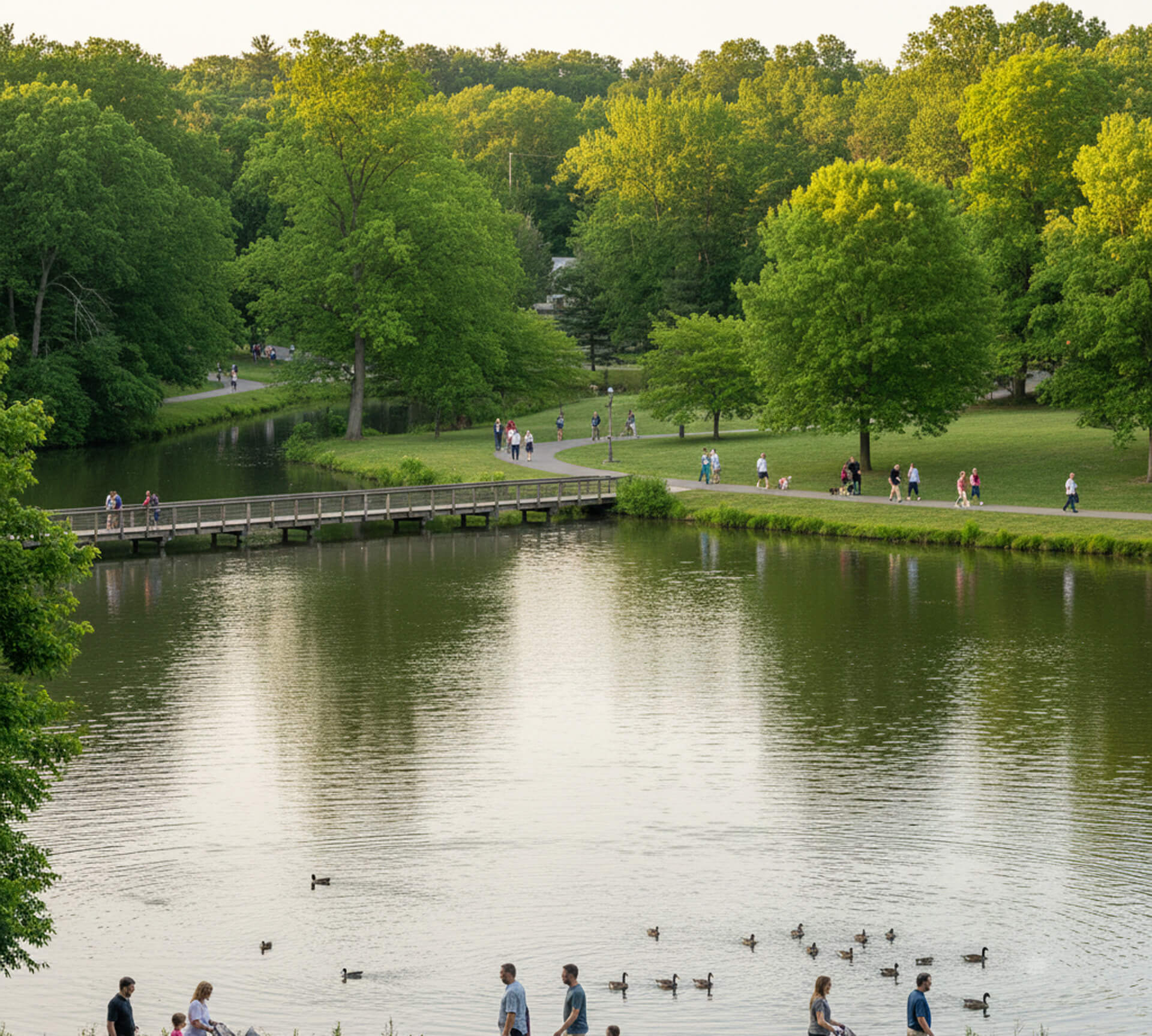 People walking along paths by a serene pond in Kennett Square, PA, surrounded by lush greenery and ducks swimming in the water, reflecting a family-friendly atmosphere.