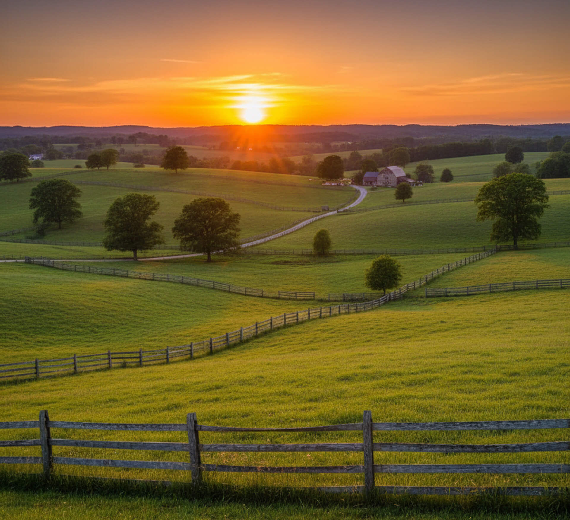 Sunset over lush green fields with a winding dirt road, wooden fences, and a distant farmhouse in Marshalton, PA, reflecting the family-friendly atmosphere of M.Y. Family Dentistry.