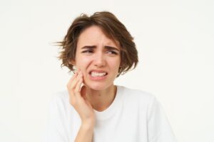 Close up of woman has a toothache touches her teeth and frowns from painful discomfort stands over