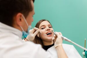 Dentist performing a professional dental cleaning while examining a female patient during a routine preventive dentistry appointment.