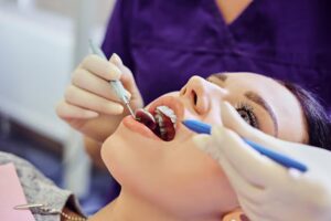 Dentist examining a woman’s teeth with dental instruments during an oral examination.